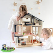 Two children playing with a wooden dollhouse on a white floor.