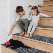 Two children sitting on a set of stairs with a black cat and a red ball.